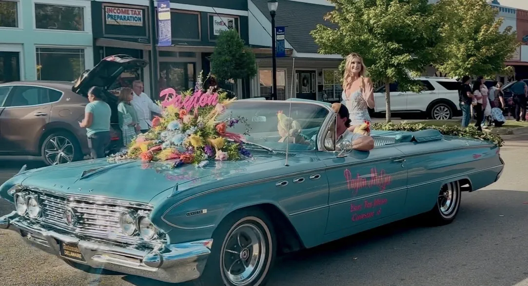 Homecoming queen waving from a blue classic convertible in a downtown parade