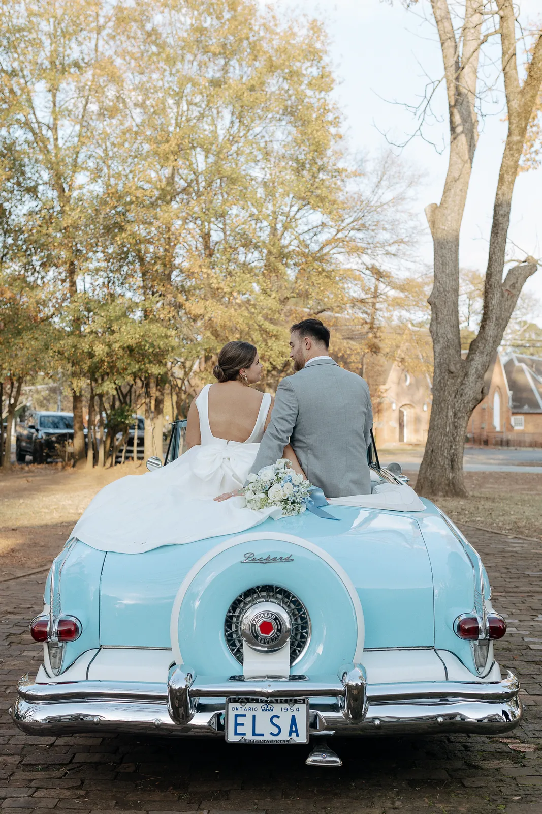 Bride and groom on the back of a light-blue classic Packard convertible